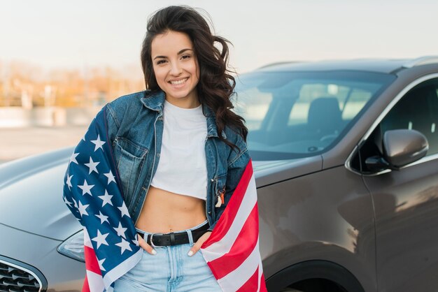 車の近くの大きなアメリカの国旗を着て半ばショットの若い女性