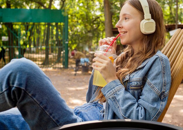 フレッシュジュースを飲むヘッドフォンでミディアムショットの若い女性