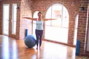 Free photo middle age beautiful sportswoman smiling happy streching using fitness ball in a class of yoga at gym