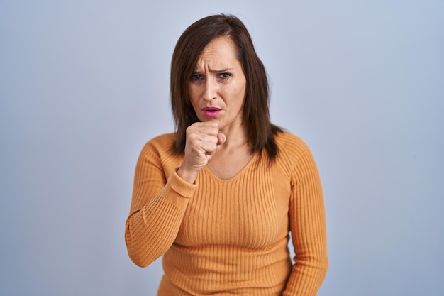 Middle age brunette woman standing wearing orange sweater feeling unwell and coughing as symptom for cold or bronchitis health care concept