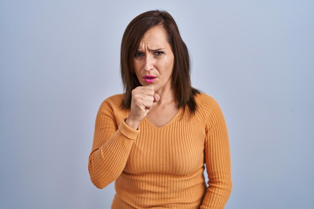 気分が悪く、風邪や気管支炎の健康管理の概念の症状として咳をするオレンジ色のセーターを着て立っている中年のブルネットの女性