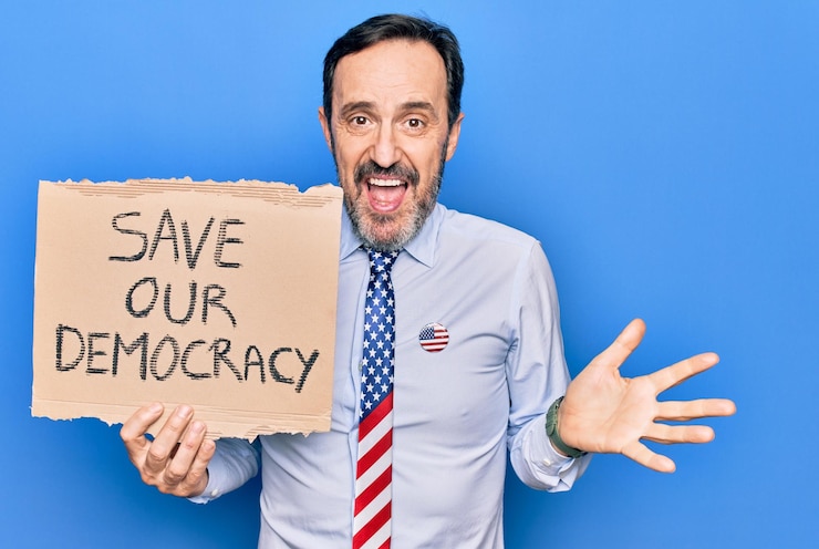 मुफ़्त फोटो middle age business man wearing usa tie holding banner with save our democracy message celebrating achievement with happy smile and winner expression with raised hand