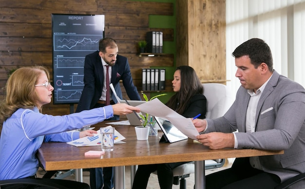 Middle age business woman giving charts to her young colleague in the conference room.