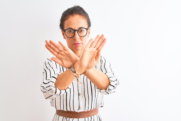 Free photo middle age businesswoman wearing striped dress and glasses over isolated white background rejection expression crossing arms and palms doing negative sign angry face