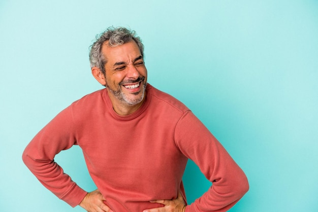 Middle age caucasian man isolated on blue background  laughs happily and has fun keeping hands on stomach.