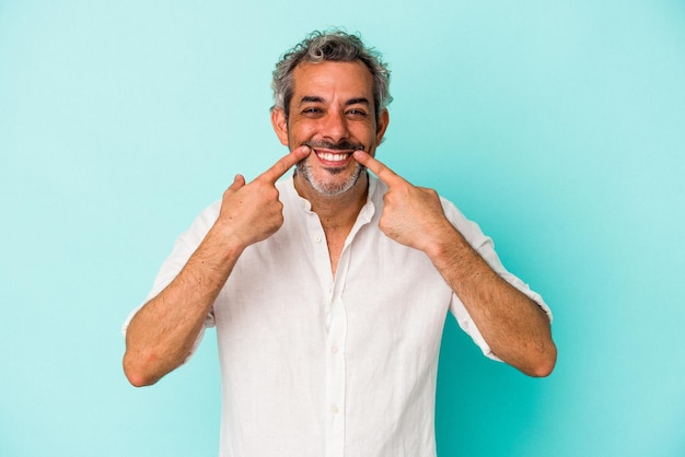 Middle age caucasian man isolated on blue background  smiles, pointing fingers at mouth.