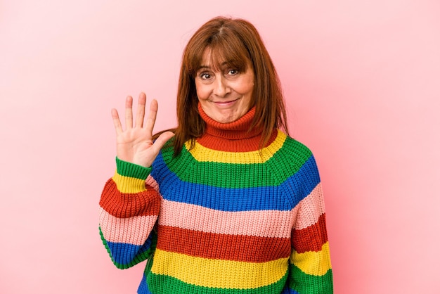 Middle age caucasian woman wearing a multicolor sweater isolated on pink background smiling cheerful showing number five with fingers.