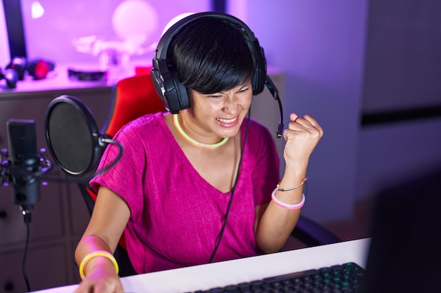 Бесплатное фото Китаянка средних лет, стримерша, играет в видеоигру с выражением победителя в игровой комнате