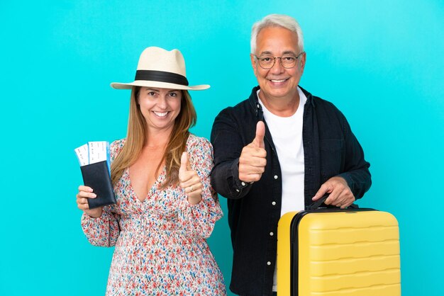 Пара среднего возраста собирается в путешествие и держит чемодан на синем фоне, показывая большой палец вверх, потому что произошло что-то хорошее