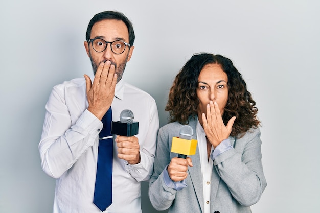 Free photo middle age couple of hispanic woman and man holding reporter microphones covering mouth with hand shocked and afraid for mistake surprised expression