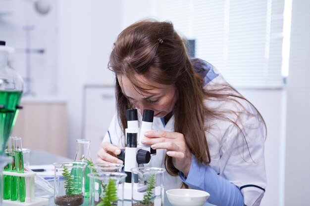研究室で顕微鏡を通して見ている中年の女性科学者。バイオテクノロジー研究所。