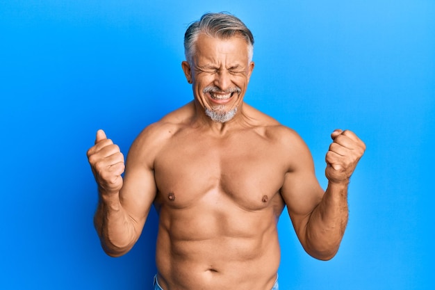 Middle age grey-haired man standing shirtless very happy and excited doing winner gesture with arms raised, smiling and screaming for success. celebration concept.