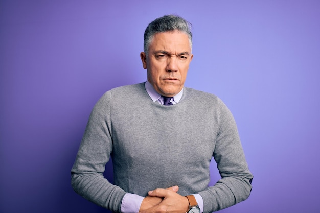 Middle age handsome greyhaired man wearing elegant sweater over purple background with hand on stomach because indigestion painful illness feeling unwell Ache concept