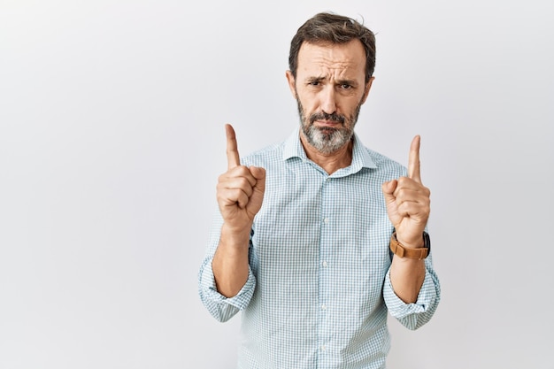 Free photo middle age hispanic man with beard standing over isolated background pointing up looking sad and upset indicating direction with fingers unhappy and depressed