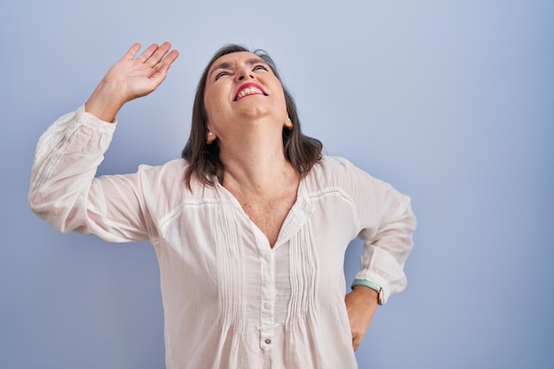 Foto gratuita donna ispanica di mezza età in piedi su sfondo blu che si allunga indietro, stanca e rilassata, assonnata e sbadigli per la mattina presto