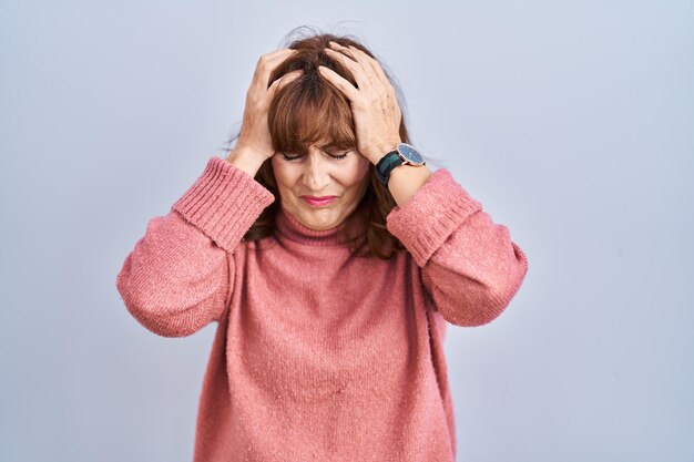 Middle age hispanic woman standing over isolated background suffering from headache desperate and stressed because pain and migraine. hands on head.