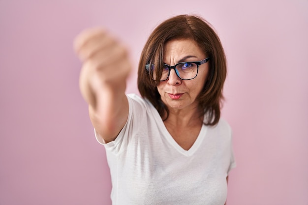 Foto gratuita donna ispanica di mezza età in piedi su uno sfondo rosa che sembra infelice e arrabbiata che mostra rifiuto e negativo con il pollice verso il basso gesto cattiva espressione