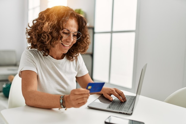 Foto gratuita donna ispanica di mezza età che utilizza il computer portatile che tiene la carta di credito a casa