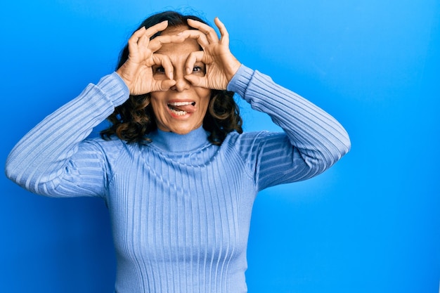 Free photo middle age hispanic woman wearing casual clothes doing ok gesture like binoculars sticking tongue out eyes looking through fingers crazy expression