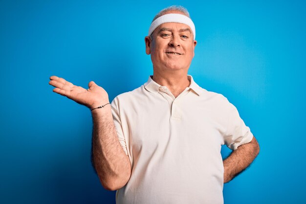 Middle age hoary sportsman doing sport wearing sportswear over isolated blue background smiling cheerful presenting and pointing with palm of hand looking at the camera