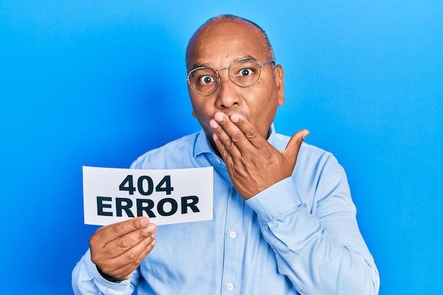 Free photo middle age latin man holding paper with 404 error message covering mouth with hand, shocked and afraid for mistake. surprised expression