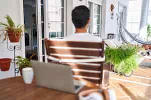 Foto gratuita uomo di mezza età che utilizza il computer portatile a casa in piedi all'indietro guardando lontano con le braccia incrociate