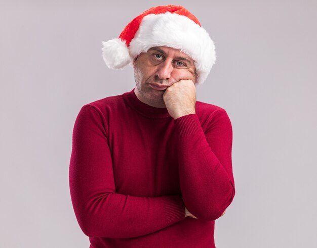 middle age man wearing christmas santa hat looking at camera tired and bored standing over white background
