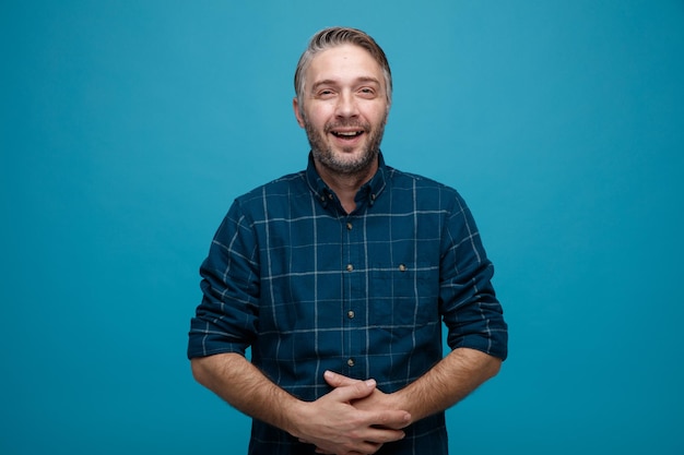 Free photo middle age man with grey hair in dark color shirt laughing out holding hands on his belly happy and joyful standing over blue background