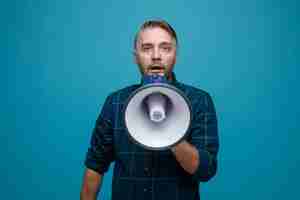 Free photo middle age man with grey hair in dark color shirt speaking in megaphone being surprised standing over blue background