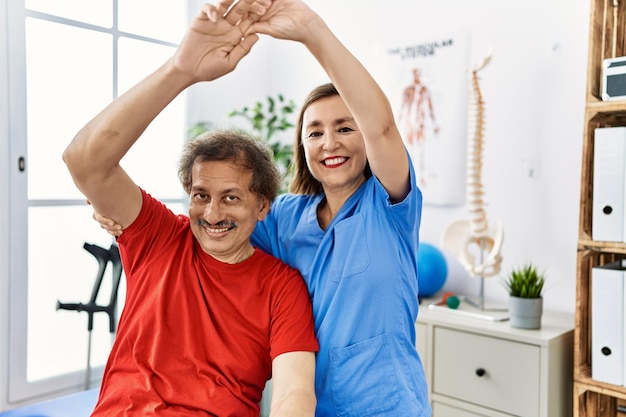 Free photo middle age man and woman wearing physiotherapy uniform having rehab session stretching arm at physiotherapy clinic