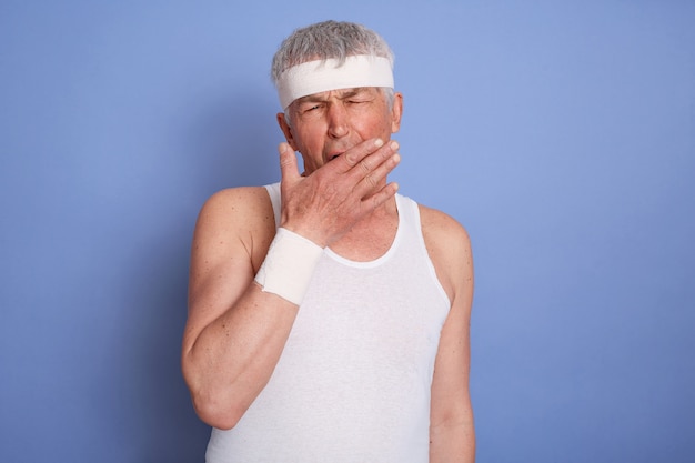 Free photo middle age sportsman being tiered after doing sport, wearing sportswear isolated, looks bored, yawning, covering mouth with hand.