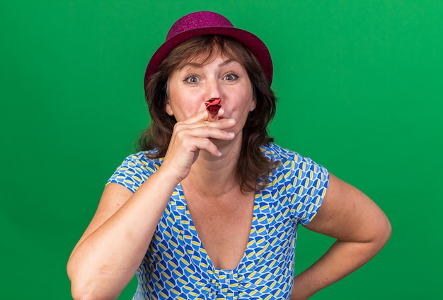 Free photo middle age woman in party hat blowing whistle happy and cheerful