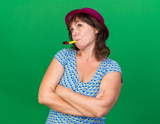 Free photo middle age woman in party hat blowing whistle looking up puzzled