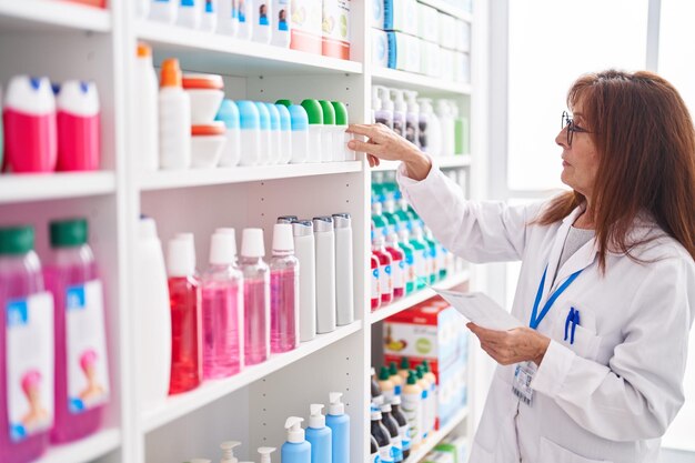 Middle age woman pharmacist holding bottle reading prescription at pharmacy