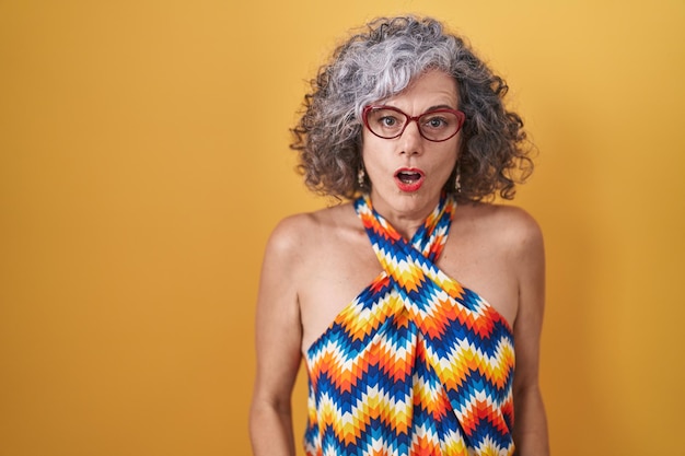 Free photo middle age woman with grey hair standing over yellow background afraid and shocked with surprise and amazed expression, fear and excited face.