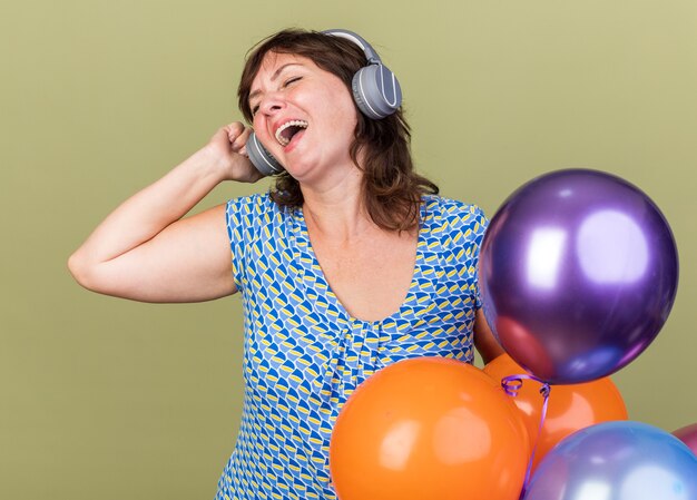 Middle age woman with headphones and bunch of colorful balloons happy and cheerful enjoying her favorite music