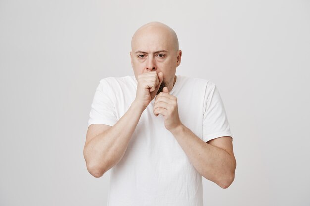 Middle-aged bald man coughing in fist