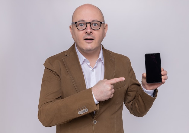 Middle-aged bald man in suit wearing glasses presenting smartphone pointing