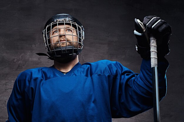 Middle-aged bearded hockey player wearing full sports equipment with a hockey stick