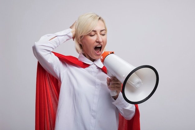 Middle-aged blonde superhero woman in red cape shouting in loud speaker looking down keeping hand on head