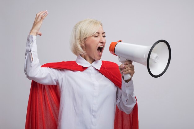 Middle-aged blonde superhero woman in red cape shouting in loud speaker looking at side raising hand up