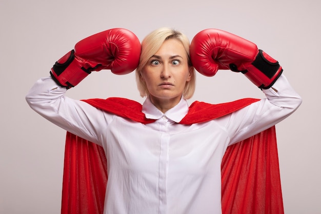 Foto gratuita donna bionda di mezza età del supereroe in mantello rosso che indossa i guanti della scatola che si batte in testa con gli occhi incrociati