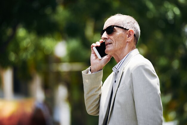 Кавказский исполнительный среднего возраста в солнцезащитные очки, говорить на смартфоне на улице