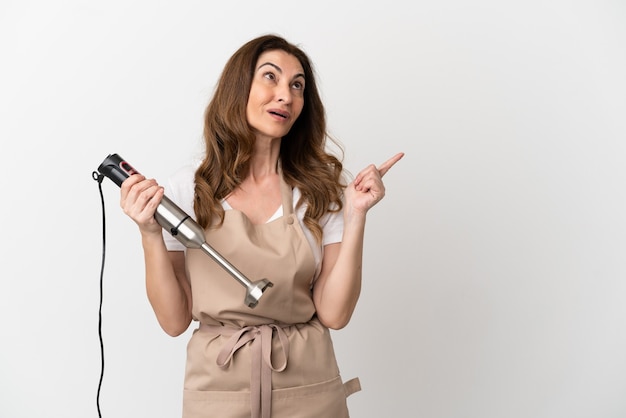 Middle aged caucasian woman using hand blender isolated on white background intending to realizes the solution while lifting a finger up