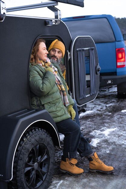 Middle aged couple rest in camper smile good mood at winter vacation in the wild Traveling across country mature couple rest in camper woman look with love on her husband Journey concept