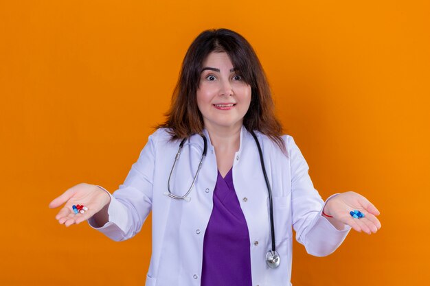 中年の医師が白いコートを着て、聴診器で錠剤を手で押し驚いて、オレンジ色の壁に笑みを浮かべて