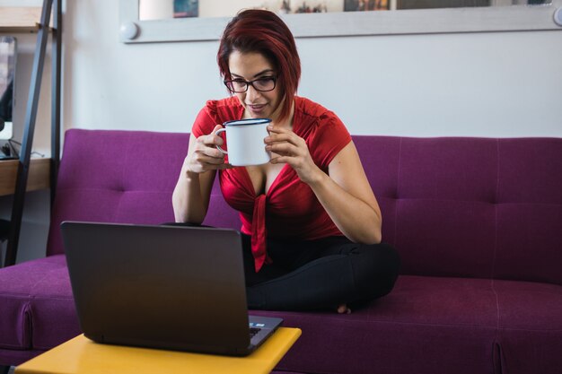 Женщина средних лет сидит с чашкой в руках и общается с помощью ноутбука
