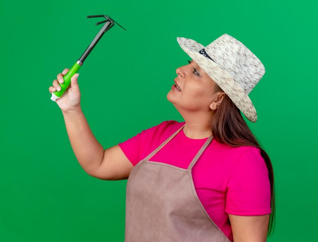 Middle aged gardener woman in apron and hat holding mattock