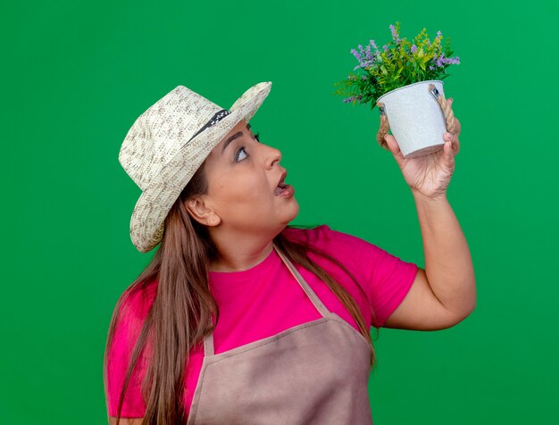 Middle aged gardener woman in apron and hat holding potted plant