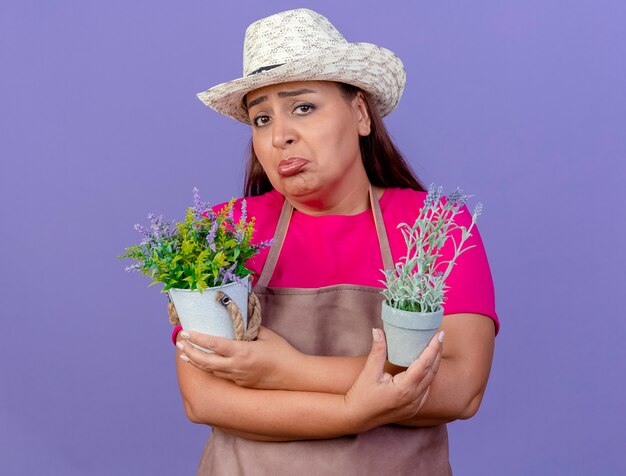 Middle aged gardener woman in apron and hat holding potted plants